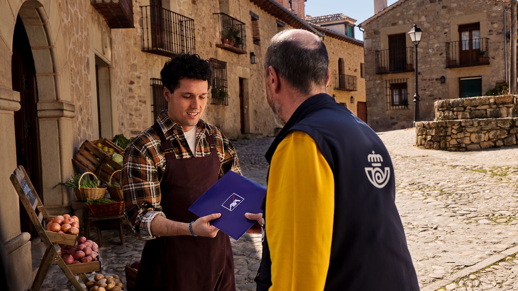 Un empleado de Correos entrega un sobre de AXA a un comerciante del pueblo, a la puerta de su tienda